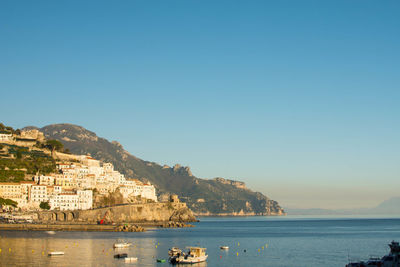 Sailboats in sea by buildings against clear sky