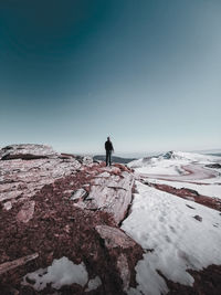 Man standing on rock looking at snowcapped mountain against sky