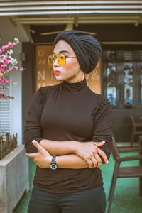 Young woman wearing sunglasses standing against cafe