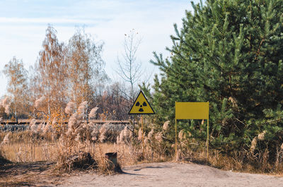 Road sign by trees on field against sky