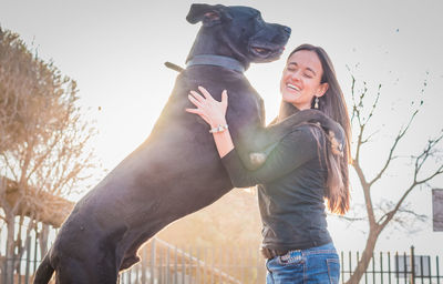 Smiling woman embracing dog against sky