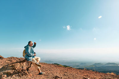 Rear view of man looking through binoculars at panoramic view of colorful summits of volcano etna.