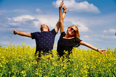 Young woman and man with arms raised by plants against sky