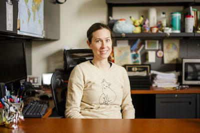 A smiling woman professor sits at her desk in an office