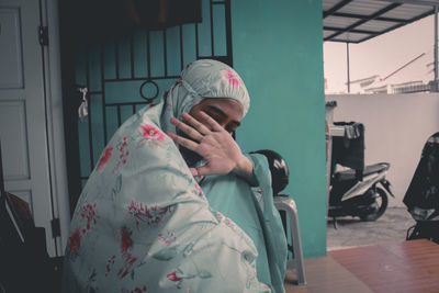 Woman covering face against house