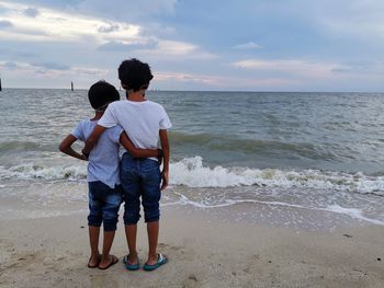 Rear view of boys standing on beach against sky