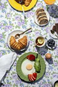 Homemade full healthy breakfast in sunlight with eggs, avocado, strawberries, blueberries, sponge cake, croissants, toast, tea, coffee and orange juice