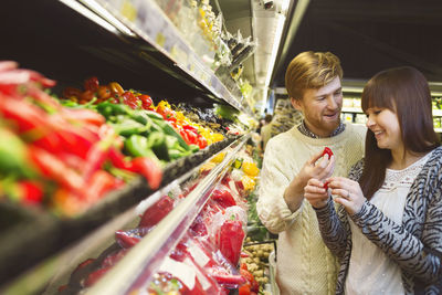 Smiling young couple discussing while buying vegetables at supermarket