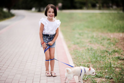 Smiling baby girl 4-5 year old walking with chihuahua pet in park. looking at camera.