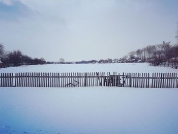 Fence on snow covered land against sky