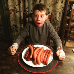 Portrait of boy with sausages in plate at table