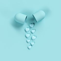 High angle view of heart shape pills by open capsule against blue background