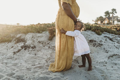 Side view of young toddler girl hugging her mother’s pregnant belly