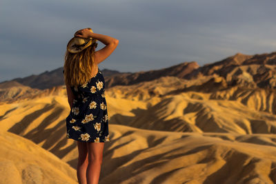 Rear view of woman standing on rock against sky