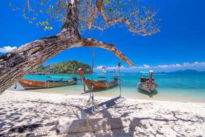 Boats moored on beach against blue sky