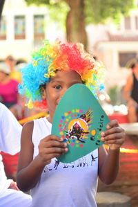 Portrait of boy wearing wig while holding card in city during event