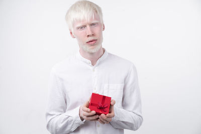 Portrait of man with albino holding christmas present against white background