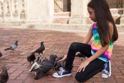 Girl feeding pigeons on city street