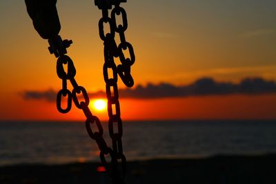 Close-up of silhouette chain hanging on beach at sunset