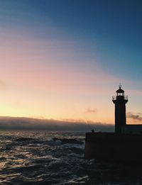 Lighthouse by sea against sky during sunset