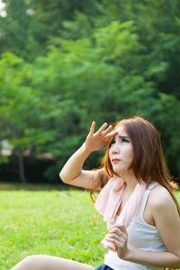 Woman shielding eyes while sitting on field