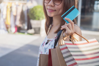 Midsection of woman holding shopping bags and credit card in city