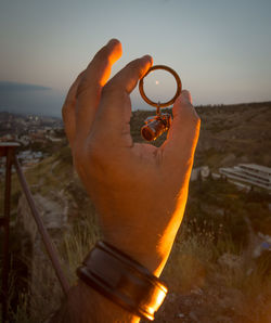 Midsection of person holding camera against sky during sunset