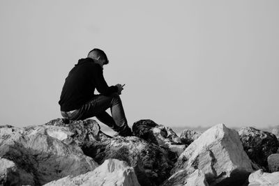 Side view of man sitting on rock against sky