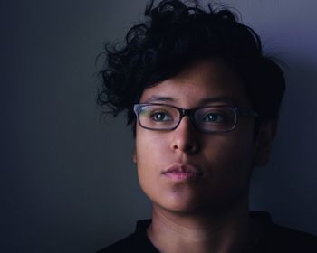 Close-up of thoughtful young woman wearing eyeglasses standing against wall