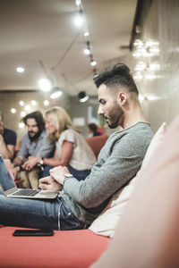 Side view of businessman working over laptop while sitting on sofa at creative office