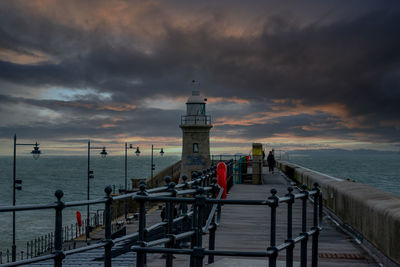 Lighthouse by sea against sky during sunset