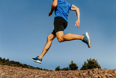 Low section of man running against clear blue sky