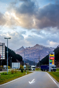 Empty road by mountains against cloudy sky