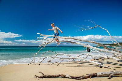 Low angle view of man standing on dead tree over sea