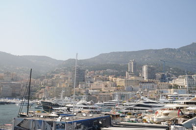 Sailboats moored at harbor by buildings in city against clear sky