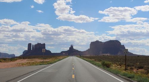 Road amidst landscape leading towards rock formations against cloudy sky