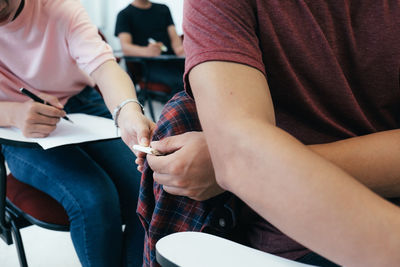 Midsection of dishonest student passing note to friend during exam in classroom
