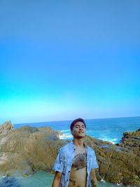 Portrait of man standing at beach against clear blue sky