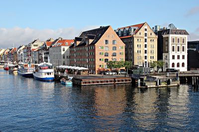 Boats moored at harbor by city against sky