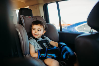 Young boy sitting in car seat wearing boxing gloves