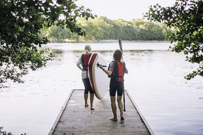 Senior women carrying paddleboard while walking on jetty towards lake