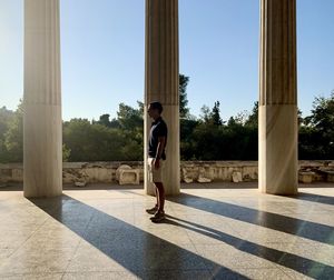 Boy standing by trees against sky on sunny day