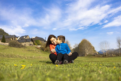 Boy kissing mother while sitting on land