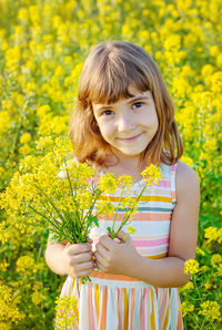 Portrait of cute girl holding flowers while standing in field