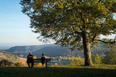 Rea view of boy and man sitting on bench at mountain