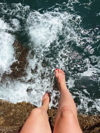 Low section of woman sitting on rocks by waterfall