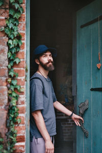 Portrait of a young man standing next to a brick wall and a green wooden door