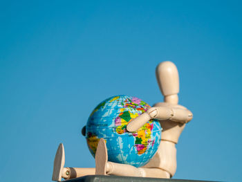 Close-up of globe and wooden figurine against clear blue sky