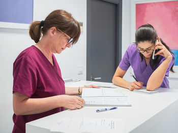 Adult women making and reading notes and answering phone call while working in modern clinic