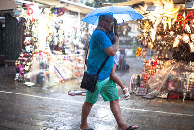 Full length of man holding umbrella on street in rainy season